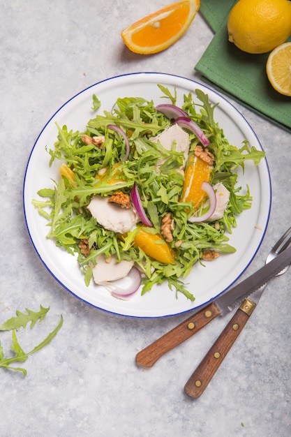 Salade biologique verte fraîche avec roquette, tranches d'orange, poulet, noix sur une plaque blanche, vue de dessus. Une alimentation saine, un régime amaigrissant concept