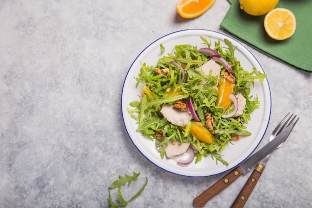 Salade biologique verte fraîche avec roquette, tranches d'orange, poulet, noix sur une plaque blanche, vue de dessus. Une alimentation saine, un régime amaigrissant concept