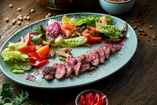 Salade de boeuf saignant moyen et de légumes frais, servie dans une assiette bleue sur fond de bois. Nourriture de restaurant.