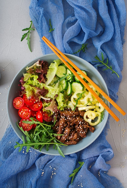 Salade de bœuf teriyaki et légumes frais - tomates, concombres, paprika, roquette et laitue dans un bol. Mise à plat. Vue de dessus