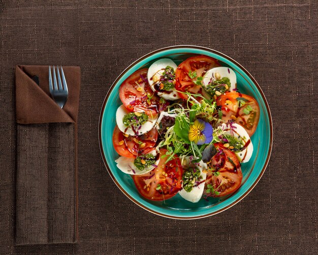 Salade Caprese sur une assiette turquoise à côté de la vue de dessus des articles de service