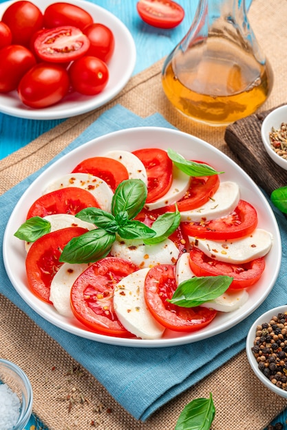 Salade caprese aux tomates, mozzarella et basilic sur fond bleu. Vue latérale, verticale.