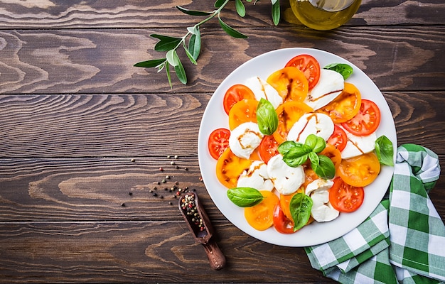 Salade caprese à base de fromage mozzarella, tomates jaunes et feuilles de basilic sur une surface en bois. Vue de dessus.