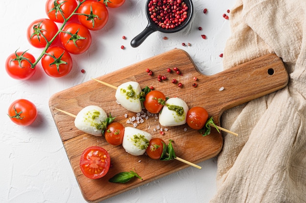 Salade caprese sur bâtonnets Tomates cerises, mozzarella, basilic, sauce pesto sur planche de bois