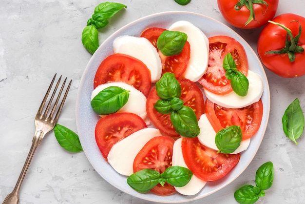 Salade caprese italienne fraîche avec tranches de tomates, fromage mozzarella, basilic, huile d'olive et fourchette dans une assiette