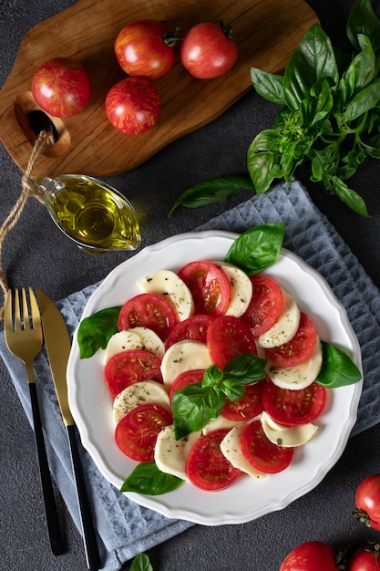 Salade caprese italienne avec tomates tranchées, fromage mozzarella, basilic et huile d'olive sur fond gris foncé. Vue d'en-haut