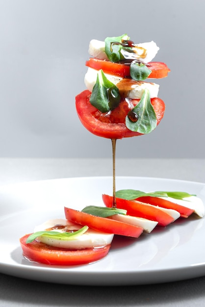 Salade caprese italienne avec tomates en tranches mozzarella basilic huile d'olive sur fond gris volant dans