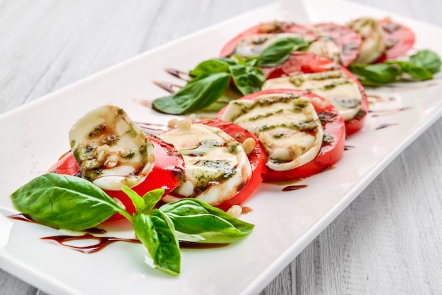 Salade caprese avec mozzarella, tomate, basilic et vinaigre balsamique disposés sur plaque blanche