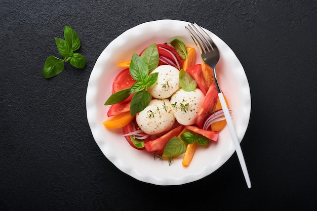 Salade caprese Salade caprese italienne avec tranches de tomates fromage mozzarella basilic huile d'olive dans une assiette blanche sur fond noir Délicieuse cuisine italienne Vue de dessus Style rustique