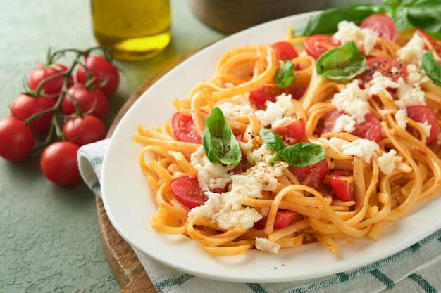 Salade caprese ou spaghetti de pâtes cassées avec basilic et mozzarella ala caprese sur plaque blanche sur fond de bois rustique vert Cuisine italienne traditionnelle Concept de cuisine italienne Vue de dessus Recette