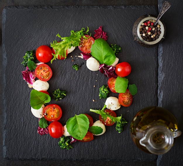 Salade caprese tomate et mozzarella au basilic et fines herbes sur fond noir.