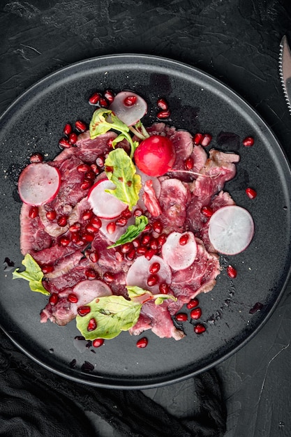 Salade de carpaccio frais avec vinaigre de vin serti de radis et grenat sur plaque sur fond de pierre noire vue de dessus mise à plat