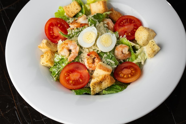 Salade César aux crevettes grillées tomate œuf bouilli croûtons de laitue et sauce verte Vue de dessus gros plan sur une assiette ronde brune avec des légumes frais