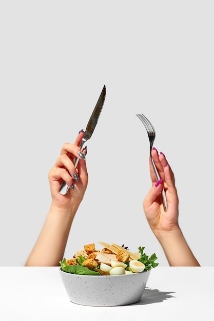 Salade César aux croûtons Les mains d'une femme avec un couteau et une fourchette sortent de sous la table Creative
