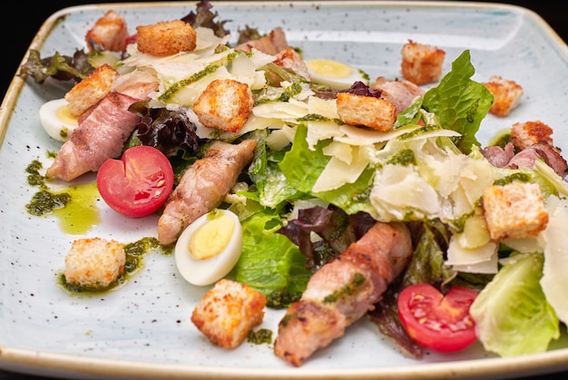 Salade César aux herbes, œufs de bacon de poulet et tomates sur une assiette lumineuse carrée sur fond sombre