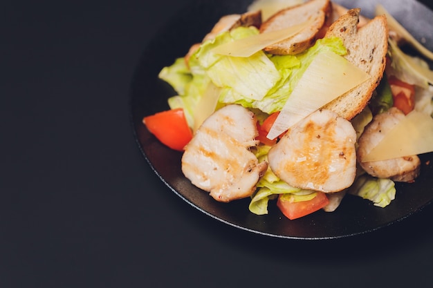 Salade César classique avec poitrine de poulet grillée et moitié d'oeuf dans une assiette en céramique blanche. Servi avec des ingrédients ci-dessus sur le vieux fond en bois bleu foncé. Vue de dessus, espace.