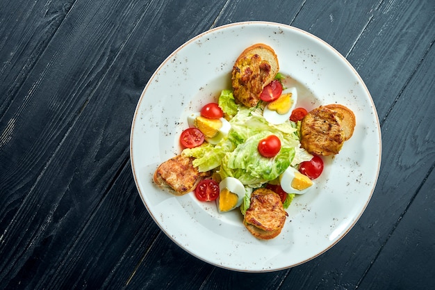 Salade César avec croûtons, parmesan, bacon, poulet, œuf en plaque noire sur une surface en bois. Service au restaurant. Gros plan avec espace de copie.