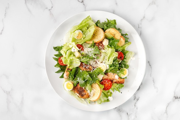 Salade césar avec croûtons de tomates à la viande de poulet rôti et fromage parmesan en assiette blanche