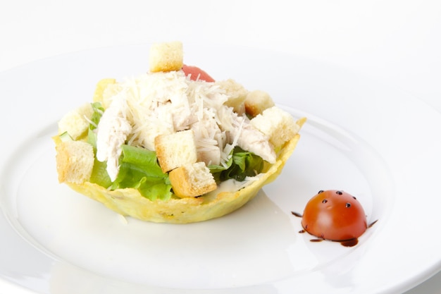 Salade César dans un panier avec tomate cerise sur une plaque blanche