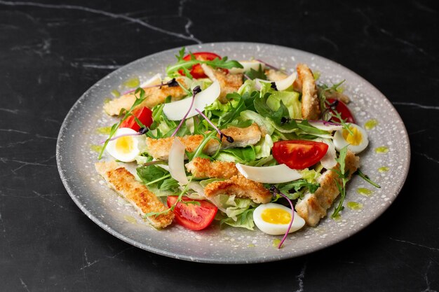 Une salade César avec des poitrines de poulet grillées des croûtons de laitue des œufs des tomates cerises habillées de parmesan et de sauce