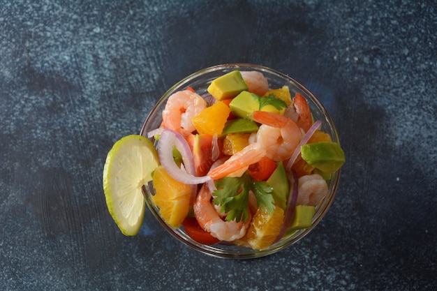 Salade de ceviche aux crevettes, oranges et avocat dans un bol en verre sur fond sombre ou gris. Cuisine latino-américaine. Délicieux ceviche de crevettes fraîchement préparé. Crevettes marinées au citron vert et à l'orange.