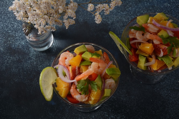 Salade de ceviche aux crevettes, oranges et avocat dans un bol en verre sur fond sombre ou gris. Cuisine latino-américaine. Délicieux ceviche de crevettes fraîchement préparé. Crevettes marinées au citron vert et à l'orange.