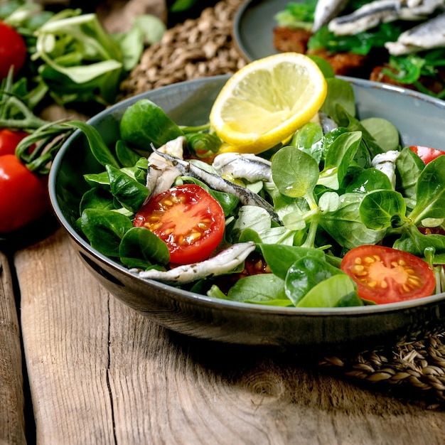 Salade de champ vert aux anchois marinés ou filet de sardines et tomates cerises, servie dans un bol bleu avec du citron et de l'huile d'olive