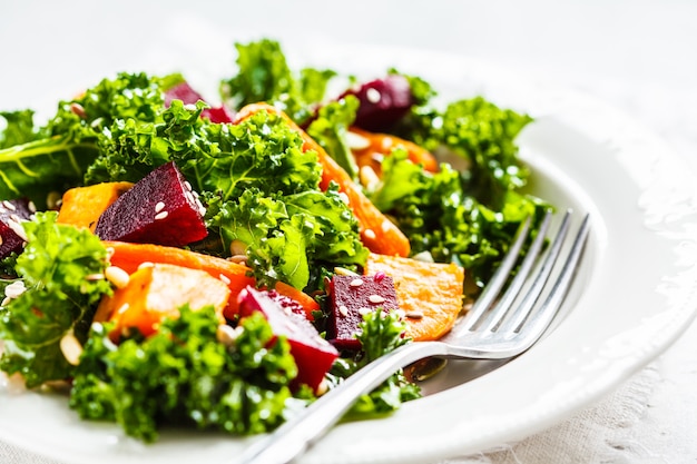 Salade de chou frisé avec des légumes cuits au four dans une assiette blanche.