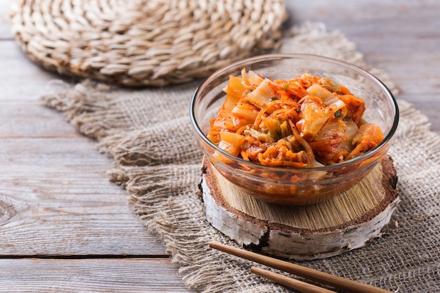 Salade de chou kimchi traditionnel bio fait maison avec des baguettes sur une table en bois. Végétarien fermenté, concept d'aliments santé intestinaux préservés végétaliens