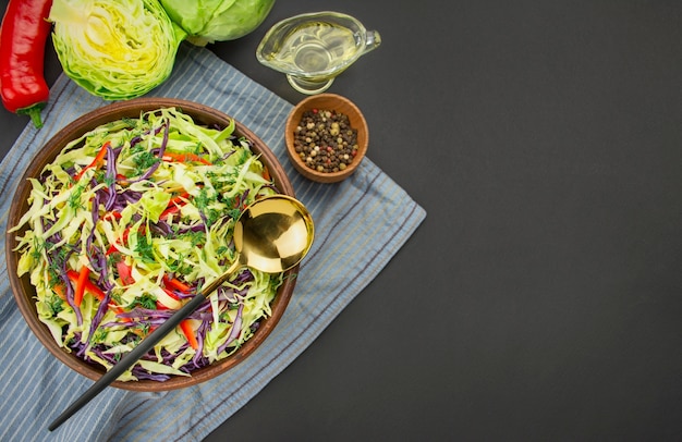 Salade de chou violet, chou blanc et poivrons dans un bol en argile foncé sur fond sombre