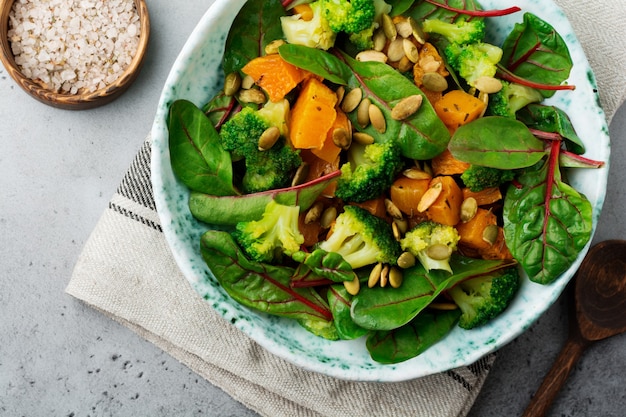 Salade avec une citrouille cuite au four, des blettes, du brocoli et des graines de citrouille dans une assiette en céramique sur une table en pierre ou en béton. Style rustique.