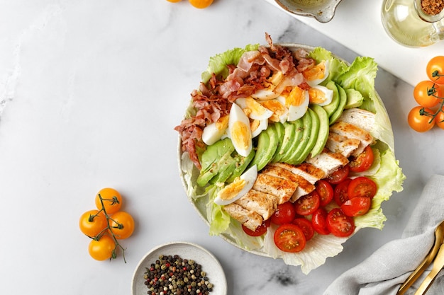 Salade Cobb aux œufs de poule grillés avocat tomate bacon sur fond blanc en marbre régime Keto