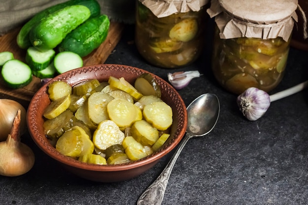 Salade de concombre mariné dans un bol et bocaux sur fond noir