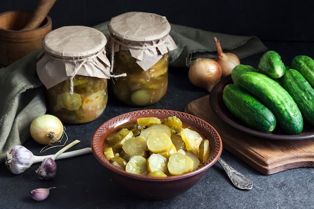 Salade de concombre mariné dans un bol et bocaux sur fond noir