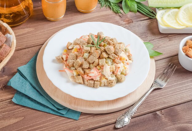 Salade de concombres de viande de poulet et croûtons assaisonnés de mayonnaise dans une assiette blanche sur un fond en bois foncé