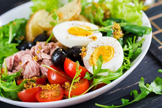 Salade copieuse et saine de thon, haricots verts, tomates, œufs, pommes de terre, gros plan d'olives noires dans un bol sur la table. Salade Niçoise. Cuisine française.