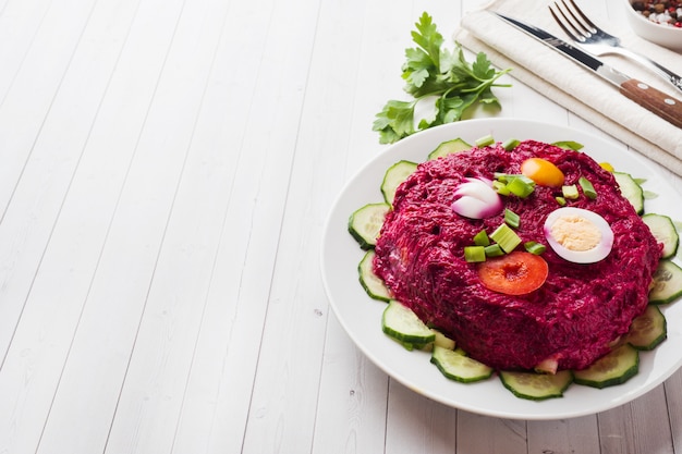 Salade en couches avec hareng et betteraves, carottes et pommes de terre et oeufs gros plan sur une assiette.