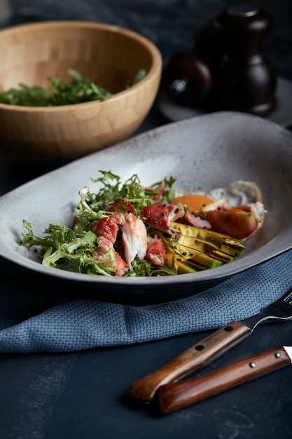 Salade de crabe et d'avocat sur fond sombre. Feuilles de salade de roquette assaisonnées de sauce au vin blanc avec chair de crabe et avocat grillé au flou.