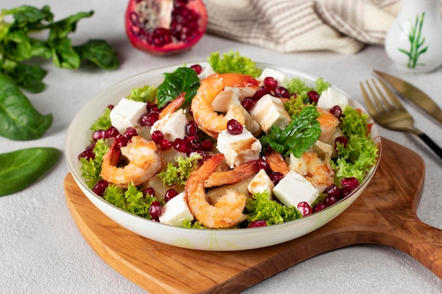 Salade de crevettes feta ananas et graines de grenade dans une assiette sur des feuilles de laitue verte sur planche de bois