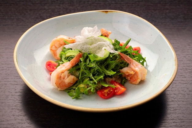 Salade de crevettes, tomates et roquette, sur une plaque blanche, sur fond sombre