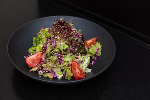 Salade dans une assiette noire sur un fond en bois noir