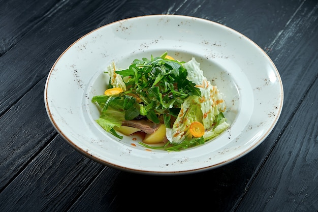 Salade diététique appétissante avec roquette, sauce, laitue et boeuf chaud dans une assiette blanche sur fond de bois sombre.