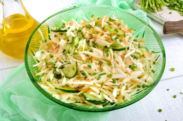 Salade diététique au chou, concombre, carotte, légumes verts. Salade de printemps juteuse de légumes frais sur un fond en bois blanc. Nutrition adéquat.