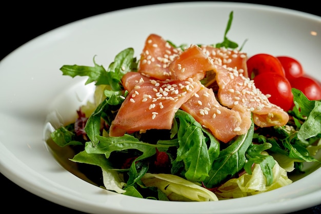 Salade diététique aux tomates et au saumon dans une assiette blanche sur fond noir