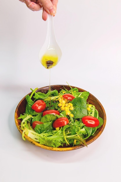 Photo salade du jardin dans un bol en bois avec sauce au goutte-à-goutte tomates maïs et laitue sur fond blanc