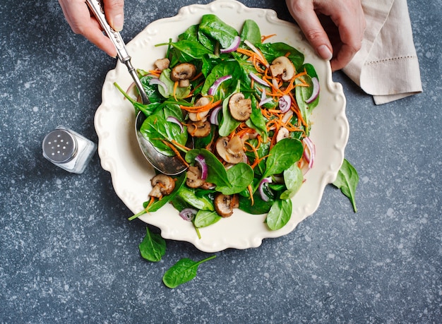 Photo salade d'épinards aux champignons et carottes. salade à main féminine