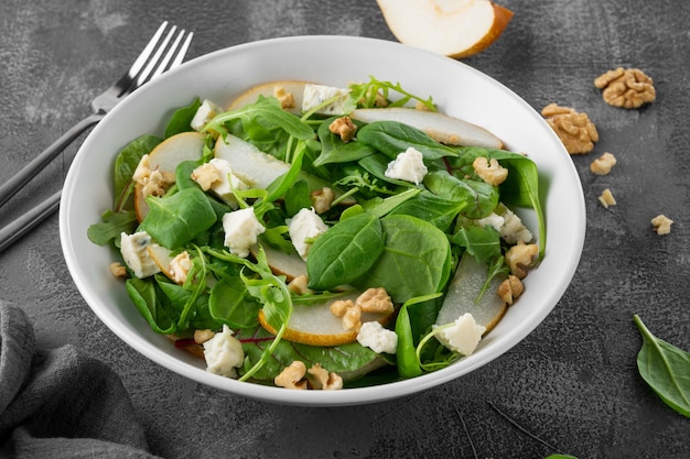 Salade avec des épinards, de la roquette, des noix de poire fraîches et du fromage gorgonzola avec de l'huile d'olive dans un bol