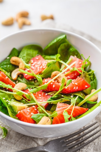 Salade d&#39;été aux fraises et aux avocats avec noix de cajou dans un bol blanc.