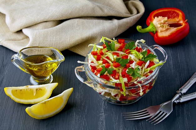 La salade d'été est un apéritif léger de chou blanc et de poivrons avec du persil dans un bol en verre sur une table en bois sombre entourée d'ingrédients