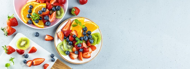 salade d'été fraîche de divers fruits et baies. Kiwi, orange, fraise et myrtille sur une assiette décorée de menthe sur une vue de dessus de table.